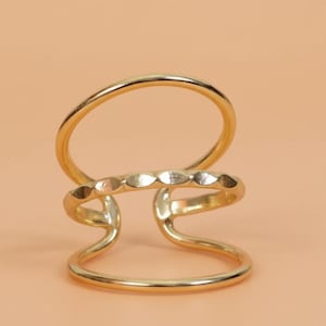 May include: A gold-colored ring with a unique design. The ring features three bands: a top circular band, a middle band with a series of diamond-shaped cutouts, and a bottom circular band. The ring has a modern, minimalist aesthetic.