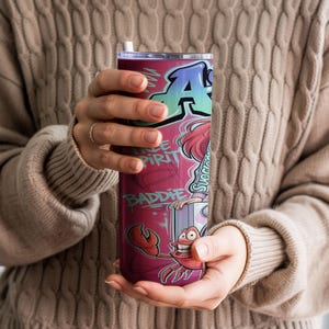Pu&ograve; includere: Un bicchiere cilindrico in acciaio inossidabile con un vivace design in stile graffiti, caratterizzato da una grande lettera A, le scritte Free Spirit e Baddie e un'illustrazione di un granchio in tonalit&agrave; rosso, rosa e blu con coperchio.