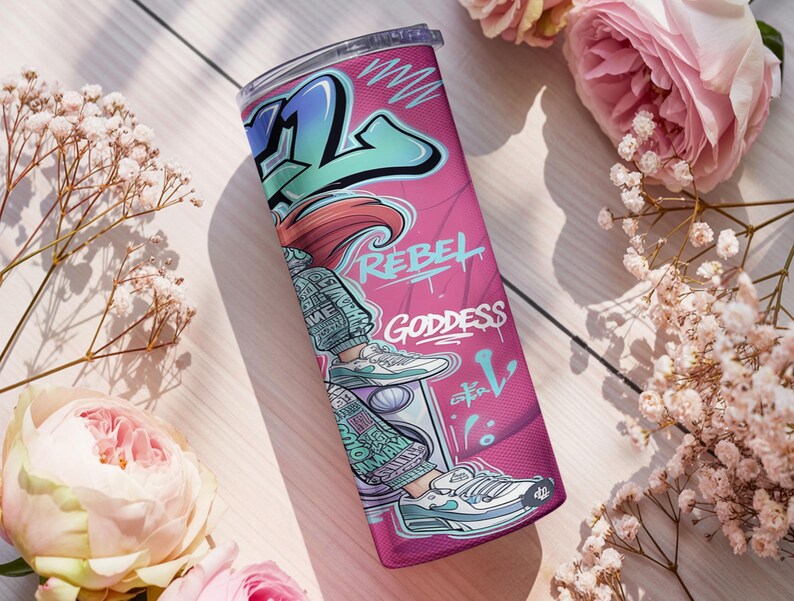 Pu&ograve; includere: Un bicchiere cilindrico con sfondo rosa e grafica in stile graffiti. Il design include una figura con scarpe da ginnastica, la scritta REBEL e GODDESS e motivi astratti blu e bianchi. Il bicchiere &egrave; dotato di un coperchio trasparente.