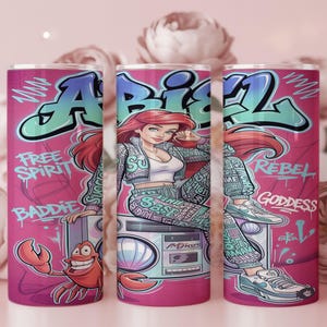 Pu&ograve; includere: Un bicchiere cilindrico con sfondo rosa caratterizzato da un'illustrazione in stile graffiti di un personaggio dai capelli rossi, che indossa giacca e pantaloni a fantasia, seduto su un boombox. Il testo include "FREE SPIRIT", "BADDIE", "REBEL" e "GODDESS".