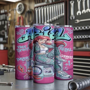 Pu&ograve; includere: Tre bicchieri cilindrici con un design graffiti rosa che raffigura un personaggio dai capelli rossi, un granchio e un boombox. Il testo recita ABIEL, FREE SPIRIT, BADDIE, REBEL e GODDESS in lettere blu e bianche su sfondo rosa vivace.