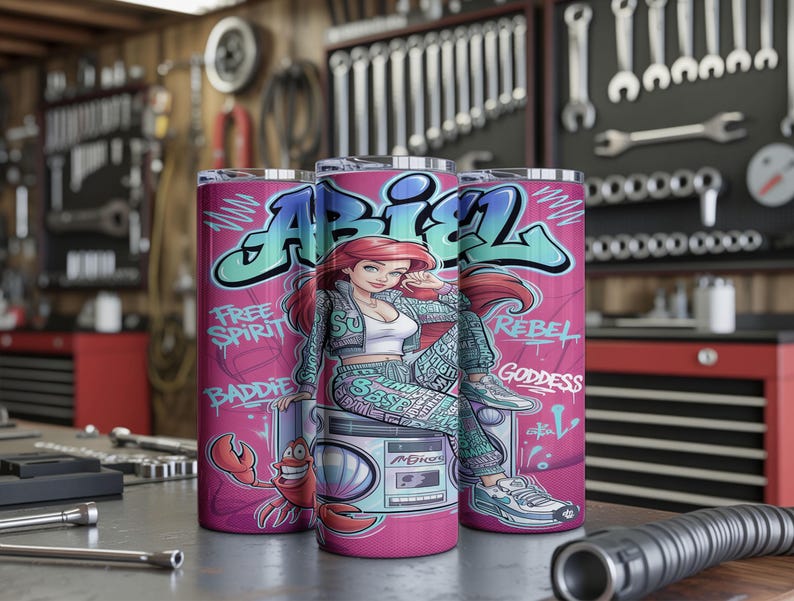 Pu&ograve; includere: Tre bicchieri cilindrici con un design graffiti rosa che raffigura un personaggio dai capelli rossi, un granchio e un boombox. Il testo recita ABIEL, FREE SPIRIT, BADDIE, REBEL e GODDESS in lettere blu e bianche su sfondo rosa vivace.