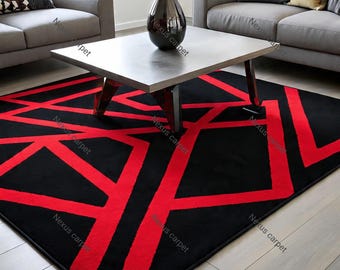 May include: A black area rug with a bold geometric design in red. The rug features a repeating pattern of thick red lines against a black background, creating a modern and striking visual effect. The rug is placed in a living room setting.