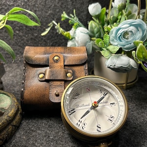 May include: A vintage brass compass with a leather case. The compass has a white face with black markings and a red needle. The leather case is brown and has a buckle closure. The compass reads "Dollond London".