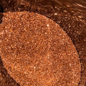 May include: Close-up of a pile of small, irregularly shaped, reddish-brown pieces. The pieces appear to be dried herbs or spices, possibly for culinary use. The image is taken from a slightly elevated angle, looking down into a container.