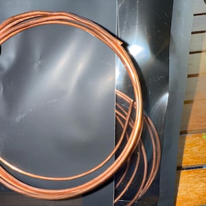 May include: Coiled copper wire, displayed against a black background. The wire has a bright, polished finish, and is arranged in loose, circular shapes. The image is well-lit, highlighting the metallic sheen of the copper.
