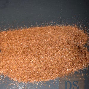 May include: A close-up shot of a pile of reddish-brown, dried tea leaves. The leaves are finely cut and appear to be loose. The background is a dark, matte surface. The image is well-lit, highlighting the texture and color of the tea.