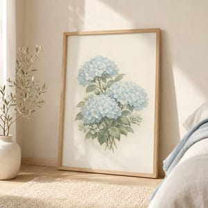 Pode incluir: Uma impressão de arte emoldurada apresentando uma ilustração botânica de três cachos de flores de hortênsia azul-claro com folhas e caules verdes, sobre um fundo branco sujo texturizado dentro de uma moldura de madeira clara.