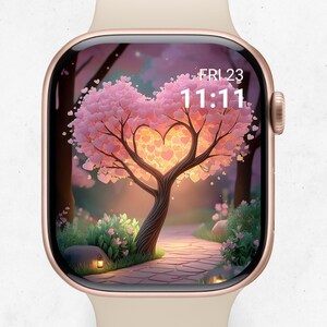 May include: A smartwatch with a screen displaying a heart-shaped tree with pink leaves and a path. The time is 11:11 on Friday the 23rd. The watch has a gold case and a light beige band.
