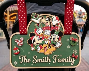 May include: A green wooden stroller sign featuring Mickey Mouse, Minnie Mouse, Donald Duck, Daisy Duck, Goofy, and Pluto in holiday attire. The sign displays the text 'The Smith Family' and is attached to a stroller with red and white polka dot straps.