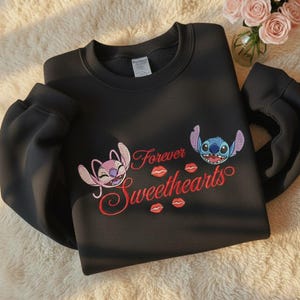 May include: Black sweatshirt featuring embroidered characters and text. The design includes two cartoon characters, pink and blue, with the words "Forever Sweethearts" in red script and red kiss marks.