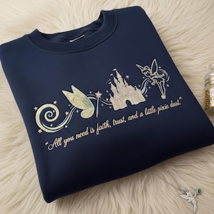 May include: Navy blue sweatshirt with embroidered design featuring a castle, fairy, and text: "All you need is faith, trust, and a little pixie dust." The design includes gold and light green accents.