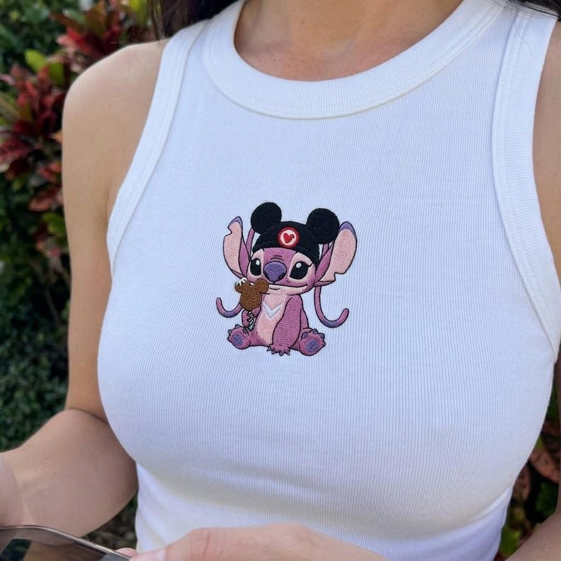 Pode incluir: Top branco canelado com um personagem de desenho animado bordado em tons de roxo, preto e castanho. O personagem usa um chap&eacute;u preto com um cora&ccedil;&atilde;o vermelho e segura um pequeno objeto.