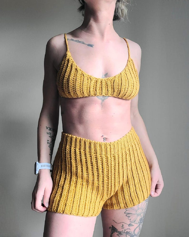 May include: Mustard yellow crochet bikini top and matching shorts set. The top has thin straps and a ribbed texture. The shorts are high-waisted with a similar ribbed design. The set is handmade and perfect for summer.