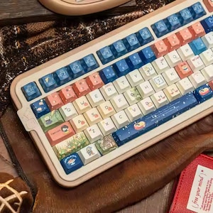 May include: A custom mechanical keyboard with a cream-colored frame and colorful keycaps. The keycaps feature a mix of pastel colors, including pink, blue, and white, with some keys displaying illustrated designs. The keyboard has a standard layout.