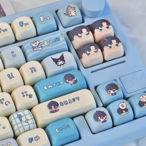 May include: A light blue mechanical keyboard with custom keycaps. The keycaps feature various cartoon characters and text, including "Back", "Enter", and "Shift". The keyboard has a light blue base and white and light blue keycaps.