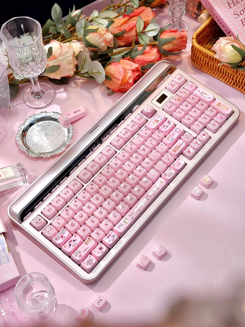May include: A pink and silver keyboard with pink keycaps decorated with cartoon animal designs. The keyboard is rectangular with a silver frame and a numeric keypad. The keycaps are decorated with various cute animal illustrations.