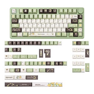 Puede incluir: Un teclado mec&aacute;nico verde menta con teclas blancas y marr&oacute;n oscuro. Las teclas presentan dise&ntilde;os celestiales y florales, con el texto "Paphiopedilum" y otros s&iacute;mbolos. Se muestran teclas adicionales debajo del teclado.