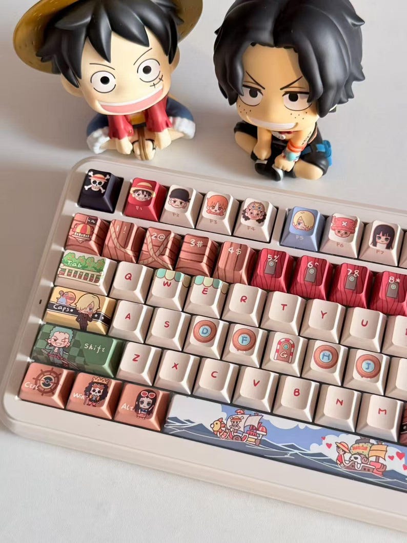 May include: A custom mechanical keyboard with keycaps featuring anime characters and imagery. The keyboard has a white frame with various colorful keycaps. Two figurines of anime characters are placed above the keyboard.