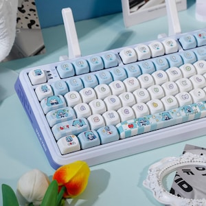Op de afbeelding: Een witte en lichtblauwe mechanische toetsenbord met aangepaste keycaps. De keycaps hebben anime-stijl illustraties in blauw en wit. Het toetsenbord heeft een lichtblauw frame en het woord "VALKYRIE" staat op de zijkant.