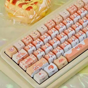 May include: A custom mechanical keyboard with light beige keys and a cream-colored frame. The keycaps feature a mix of orange and white corgi dog designs and other cute illustrations. The keyboard is angled towards the viewer.