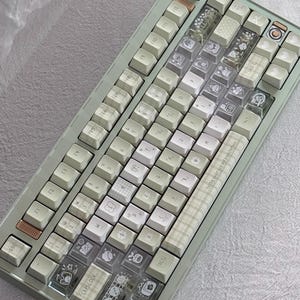 Puede incluir: Un teclado mec&aacute;nico verde menta con teclas blancas y transparentes. Algunas teclas tienen ilustraciones y patrones lindos. El teclado tiene una mezcla de teclas est&aacute;ndar y personalizadas, con el texto "Telling about lack am expectations".