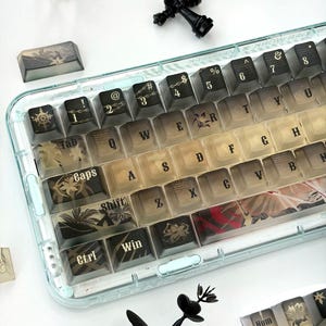 Puede incluir: Un teclado mecánico con un marco azul claro translúcido y teclas personalizadas con un degradado en negro y beige. Las teclas muestran letras blancas, motivos florales y patrones de cadenas. Una pieza de ajedrez negra y una pequeña corona están cerca.