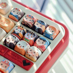 May include: A close-up of a keyboard with custom keycaps featuring cartoon character designs. The keycaps are in various colors and designs, with a red and white keyboard frame. The text "Love is a light that never dims" is visible.