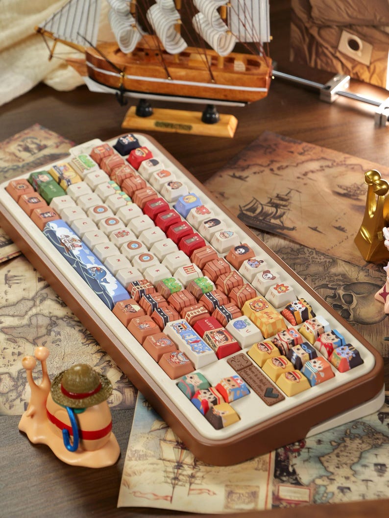 May include: A custom keyboard with keycaps featuring various cartoon characters and nautical themes. The keyboard has a brown frame and a white base. A miniature sailboat and a snail figurine are also visible.