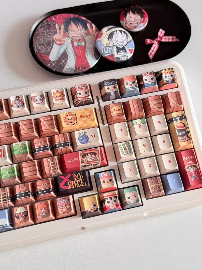 May include: A white keyboard with custom keycaps featuring cartoon characters. The keycaps are brown, white, and various colors. Above the keyboard are three round pins and a black tray with a cartoon image.