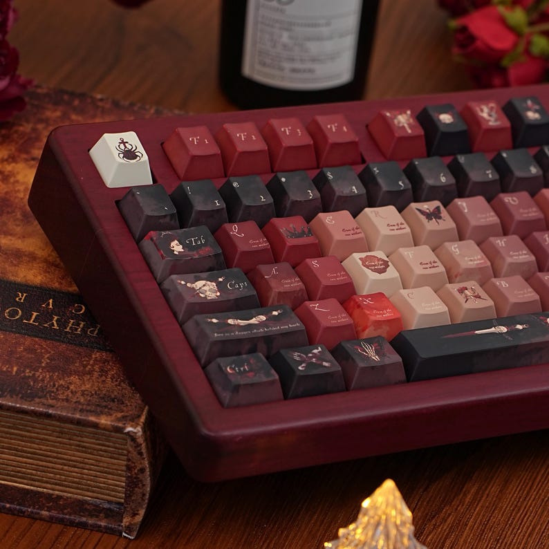 May include: A custom mechanical keyboard with a dark red wooden frame and keycaps in shades of red, black, and cream. The keycaps feature unique illustrations and text. The keyboard is angled towards the viewer, showcasing its design.