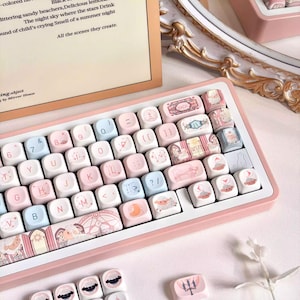 Könnte beinhalten: Eine rosa-weiße mechanische Tastatur mit individuellen Tastenkappen. Die Tastenkappen zeigen Pastellfarben und Illustrationen von Wolken, Schafen und anderen skurrilen Designs. Die Tastatur hat einen rosa Rahmen und weiße Tasten.