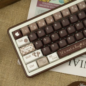 Könnte beinhalten: Eine mechanische Tastatur im Retro-Stil mit einem braunen und beigen Farbschema. Die Tastenkappen weisen eine Mischung aus braunen, beigen und weißen Tasten mit verschiedenen Symbolen und Text auf. Die Tastatur hat eine rechteckige Form und einen braunen Rahmen. Auf der Leertaste steht "It's not a bug, it's a feature".