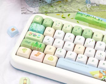 Puede incluir: Un teclado mecánico con un marco blanco y un conjunto de teclas de colores pastel. Las teclas muestran varias ilustraciones con motivos naturales, como árboles, flores y un oso, junto con caracteres alfanuméricos y símbolos estándar.