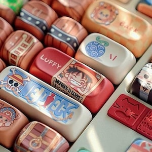 May include: A close-up of a keyboard with custom keycaps. The keycaps are decorated with various designs and characters in shades of brown, red, white, and blue. Illustrations of cartoon characters and text are visible. Some keycaps have the word "LUFFY" printed on them.