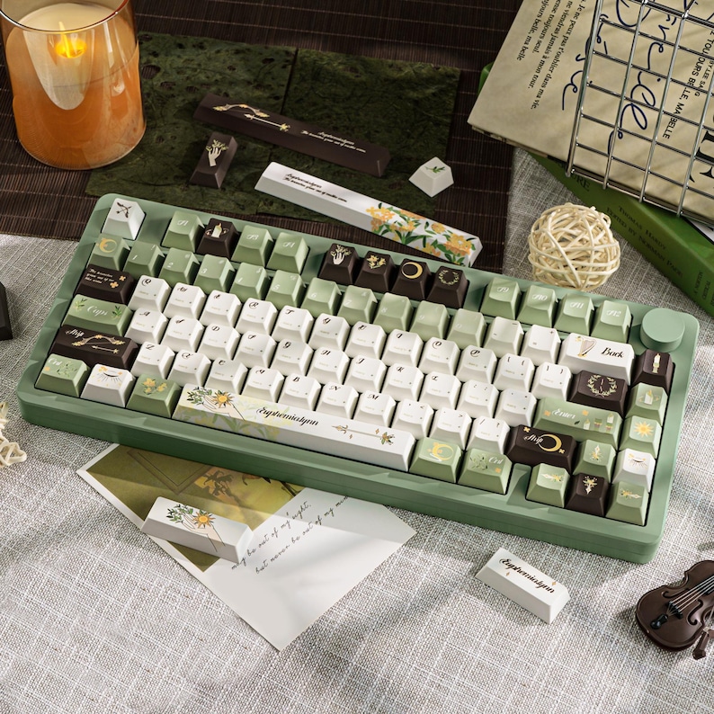 Puede incluir: Un teclado mec&aacute;nico verde y blanco con teclas personalizadas. Las teclas presentan dise&ntilde;os florales y celestiales, con la palabra "Ephemeriskyan" impresa en la barra espaciadora. El teclado tiene un marco verde y una perilla redonda verde.
