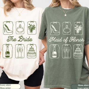 May include: Ivory and moss green t-shirts with matching ivory print designs. The ivory shirt says "The Bride" and the moss green shirt says "Maid of Honor". Each shirt features six wedding-themed illustrations.