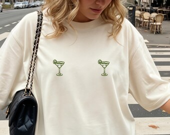 May include: Cream-colored t-shirt featuring two embroidered green margarita glasses. The casual tee has short sleeves and a relaxed fit. The shirt is made of a soft, comfortable material.