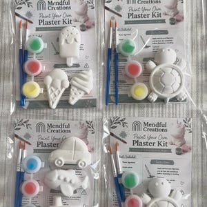 Könnte beinhalten: Vier Mendful Creations Gips-Malsets in durchsichtiger Kunststoffverpackung. Jedes Set enthält weiße Gipsfiguren, zwei Pinsel und drei kleine Farbtöpfe. Die Figuren umfassen Eiscreme, Schildkröte, Auto, Flugzeug und ein Boot.