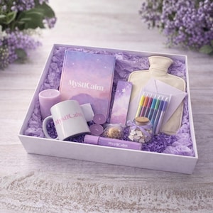 Op de afbeelding: Een witte geschenkdoos gevuld met lavendelkleurige items. Inclusief een mok, notitieboek, kaars, warmwaterkruik, pennen en een roller. De items zijn gerangschikt op paars crêpepapier. De mok en het notitieboek hebben de tekst "MystiCalm".