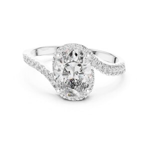 May include: A white gold engagement ring featuring an oval-cut diamond center stone surrounded by a halo of smaller diamonds. The band has a split shank design, with diamonds set along the top of the band. The ring is set against a white background.