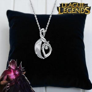 Könnte beinhalten: Eine silberfarbene Anhängerkette mit einem Blatt- und Tropfendesign und einem kleinen, funkelnden Edelstein. Die Halskette hängt an einer zarten Kette. Der Anhänger wird auf einem schwarzen Kissen präsentiert.