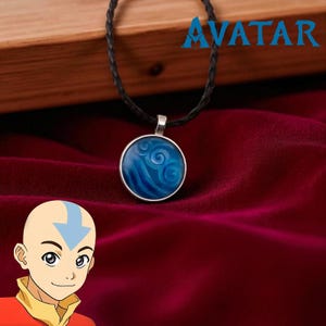 May include: A silver pendant necklace featuring a circular blue design with swirling water patterns. The pendant hangs from a black braided cord. The word "AVATAR" is displayed in blue text.