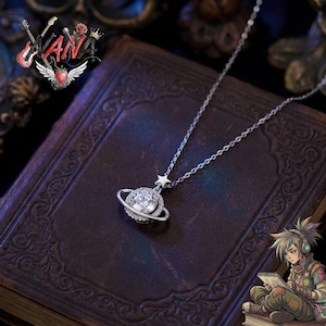 May include: A silver necklace featuring a planet pendant with a large, clear gemstone and a surrounding ring. A small star charm hangs above the planet. The necklace is displayed on a dark, textured surface.