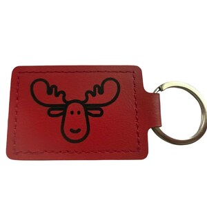 May include: Red leather keyring featuring a black cartoon moose design. The keyring has a rectangular shape with a stitched border and a silver metal ring attached.