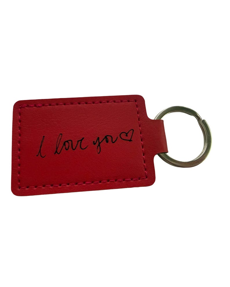May include: A red rectangular keyring with the handwritten phrase "I love you" in black script, with a heart symbol. It features a silver metal ring for attaching keys.
