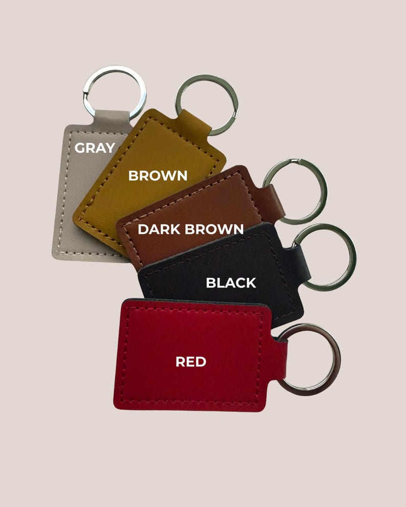 May include: A selection of rectangular keyrings in shades of grey, brown, dark brown, black, and red. Each keyring has a metal ring and the colour name printed on it.