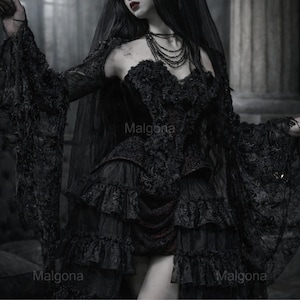 May include: A black dress featuring long flared lace sleeves, a sweetheart neckline, and a multi-layered ruffled skirt. The bodice is adorned with intricate lace detailing and floral textures. A sheer black veil is draped over the shoulders.