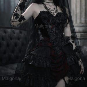 May include: A black strapless corset dress featuring intricate floral lace overlays, a layered ruffled skirt with deep red fabric accents, and matching lace arm sleeves. A sheer black veil and a multi-layered beaded necklace complete the ensemble.