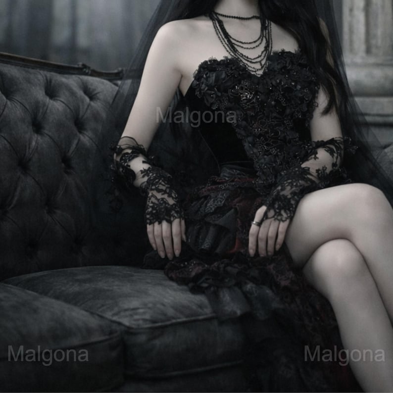 May include: A black strapless corset dress featuring intricate lace and floral embroidery, paired with matching black lace fingerless gloves, a layered tulle veil, and a multi-strand beaded necklace. The garment displays the text Malgona.